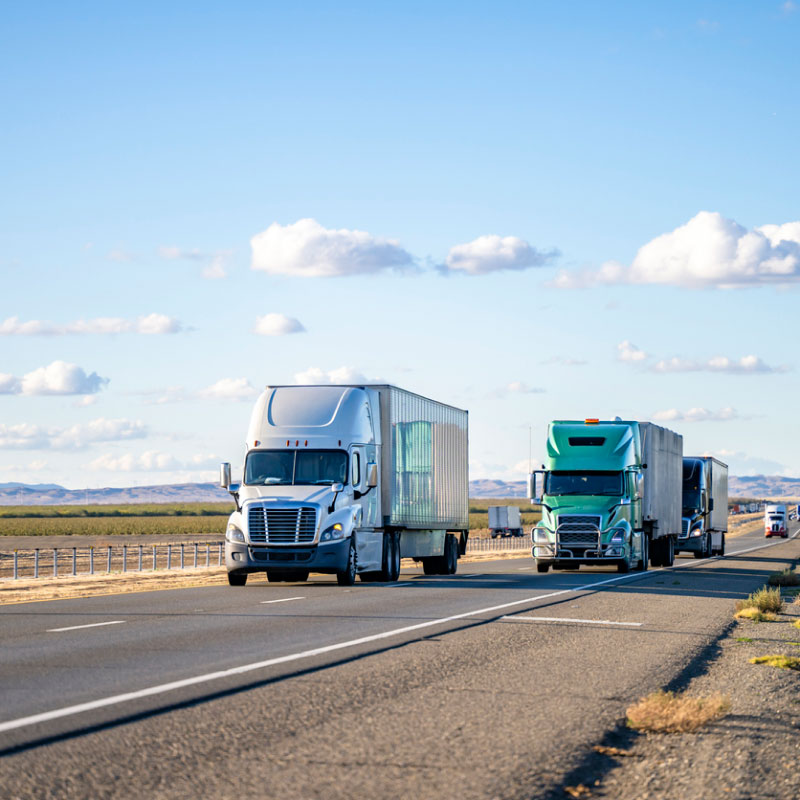 Two lanes of semi trucks driving down highway.