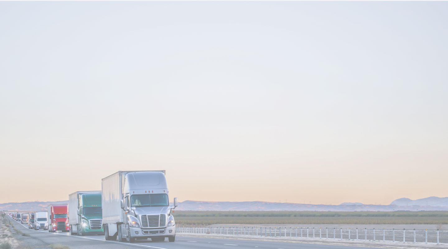 Lane of semi trucks driving down desert highway.