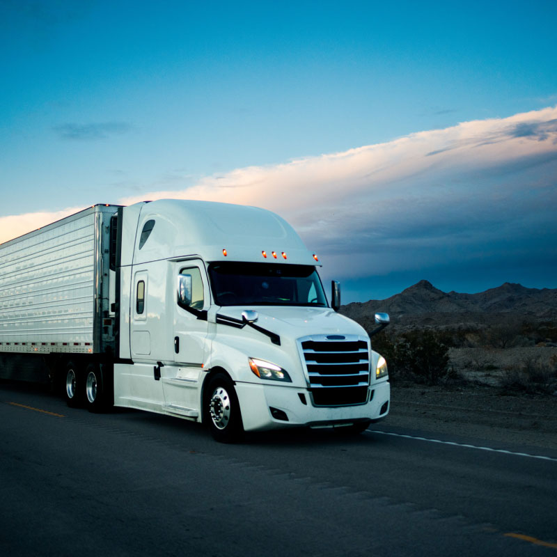 Semi truck driving down mountainous highway at dusk.