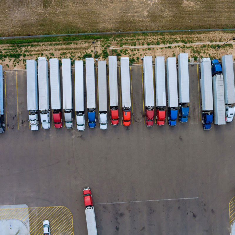 Multiple semi trucks lined up in a row at the rest stop area on a highway.