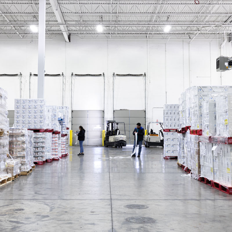 A well lit large warehouse with packaged shipments that warehouse facility members are monitoring.