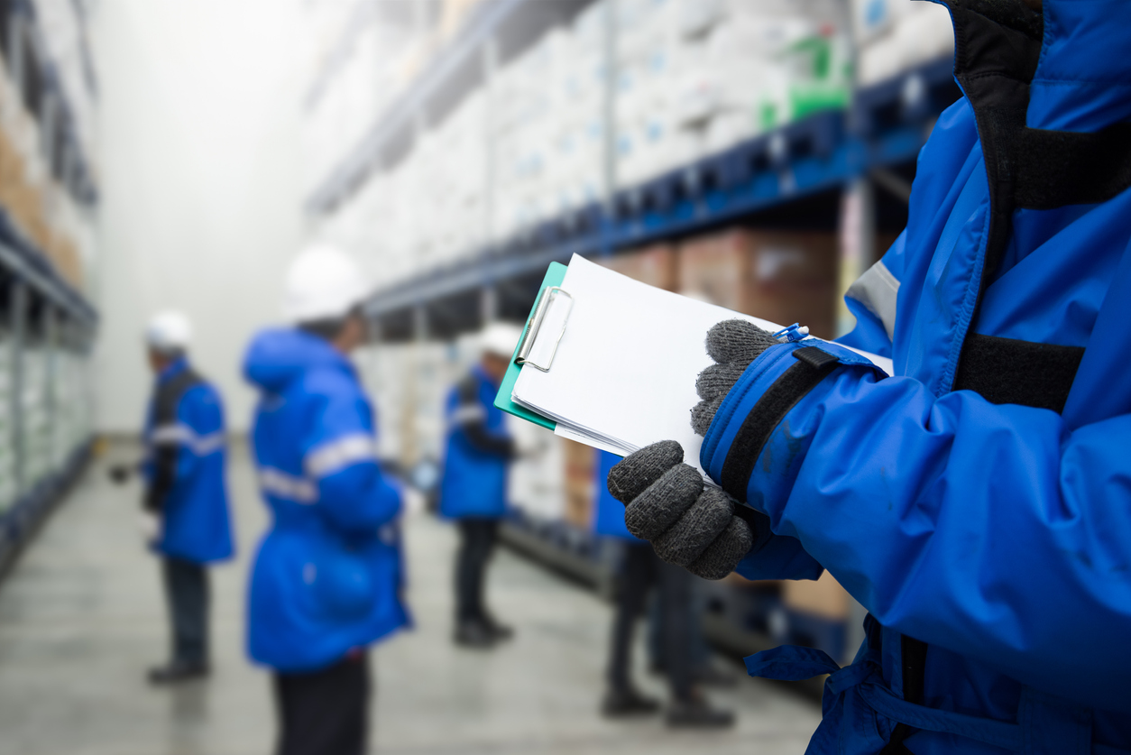 Warehouse worker with clipboard checking goods in freezing room.