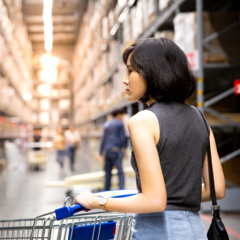 A women walking through a store with a shopping cart.