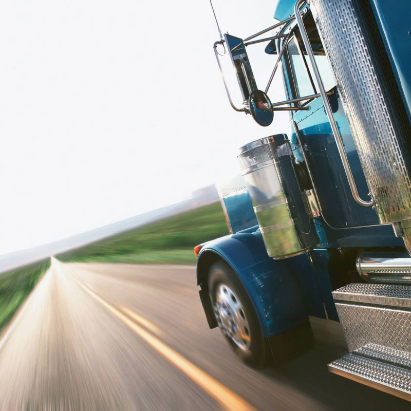 A blue semi truck speeding down a highway.