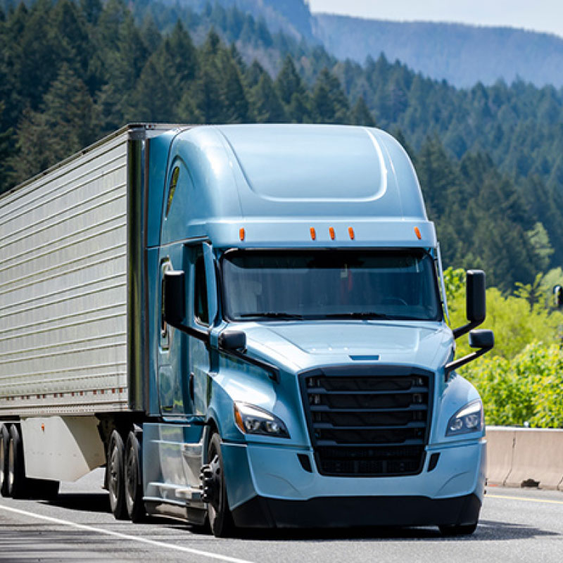 A blue semi truck driving down a highway with trees on either side.