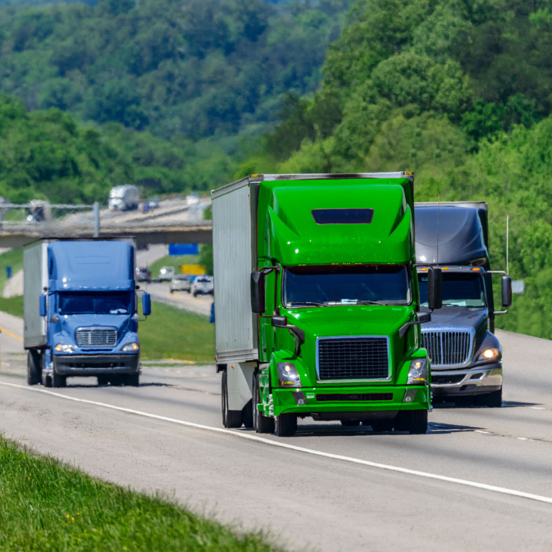 Multiple trucks driving on the highway going under a bridge in the distance.