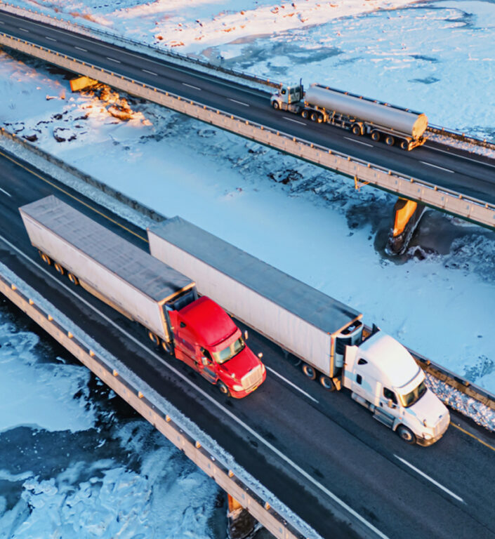 Two semi trucks driving down a highway bridge over frozen water. 