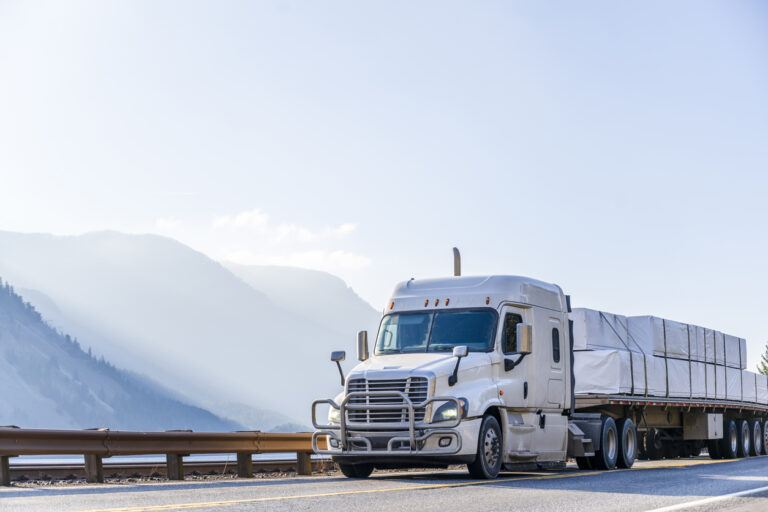 A white flatbed semi truck driving down the highway. 