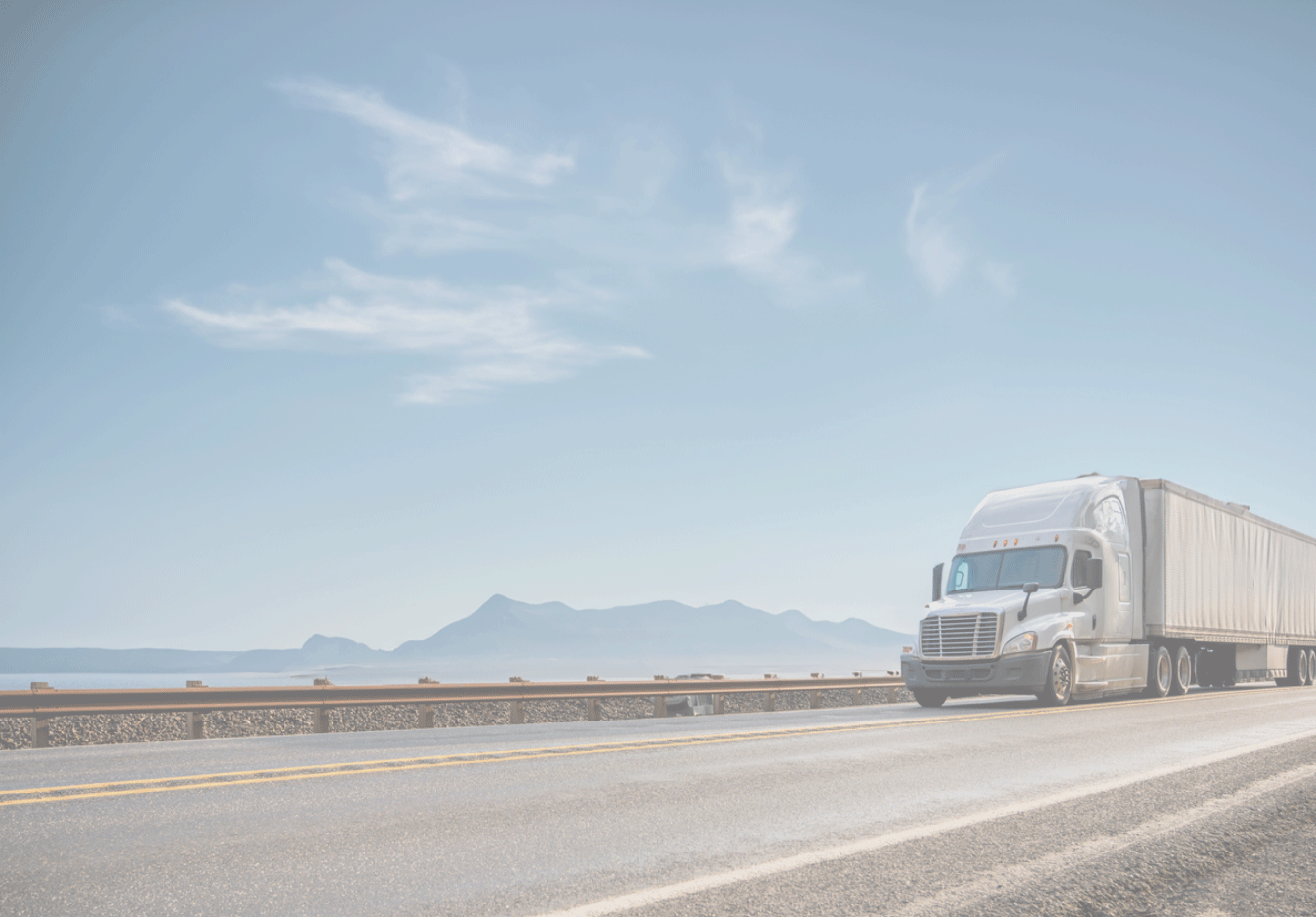 White semi truck driving along highway with mountains in the background.