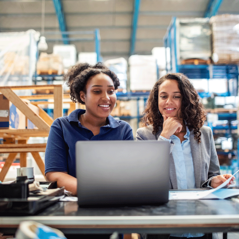 Two women on computer in warehouse.