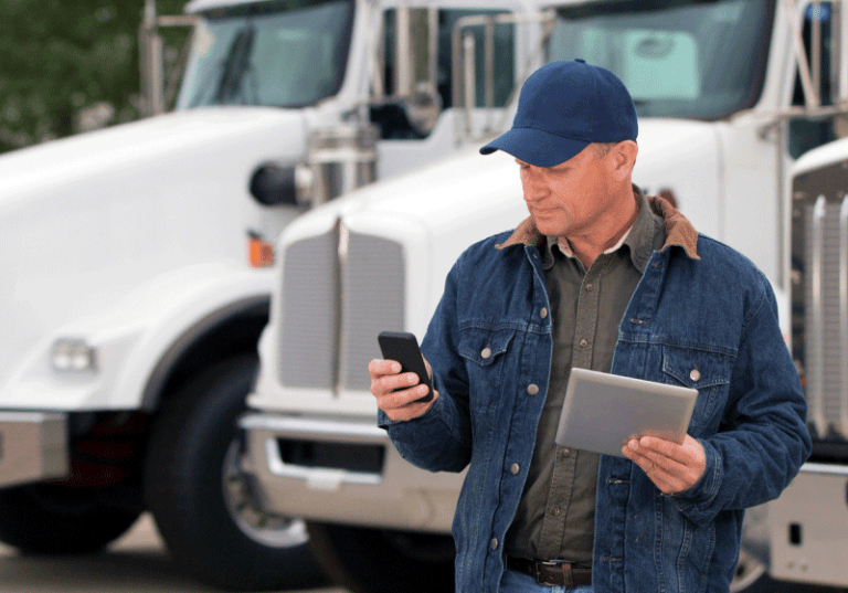 man looking at his phone in front of parked semi trucks