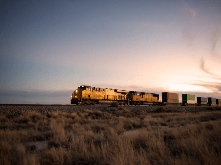 An intermodal rail car carrying brightly colored freight during a sunset.